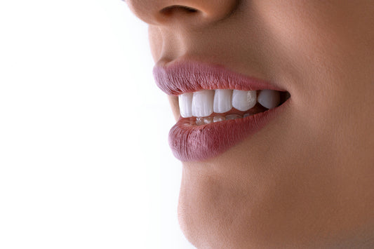 Zijaanzicht van een glimlachende vrouw met volle roze lippen en stralend witte tanden, gefotografeerd tegen een witte achtergrond voor een frisse en hygiënische uitstraling.