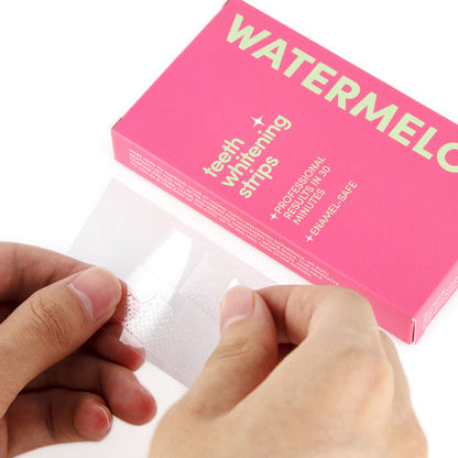 Handen die een Lucid Bite Watermelon tanden whitening strip vasthouden naast de roze-watermeloen verpakking.